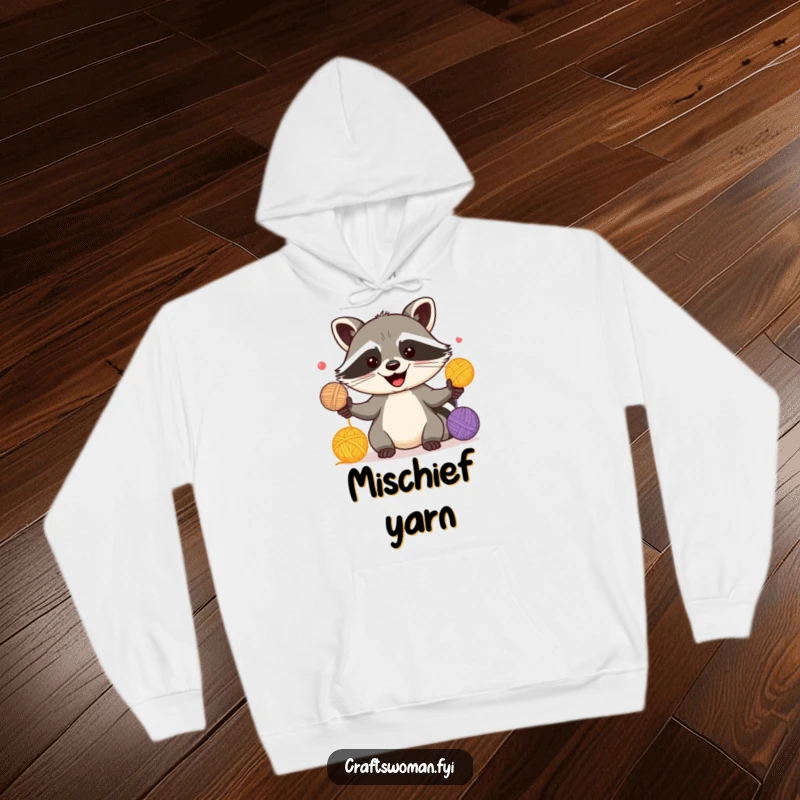 Funny hoodie featuring a happy raccoon juggling colorful yarn balls, perfect for cozy knitting moments.