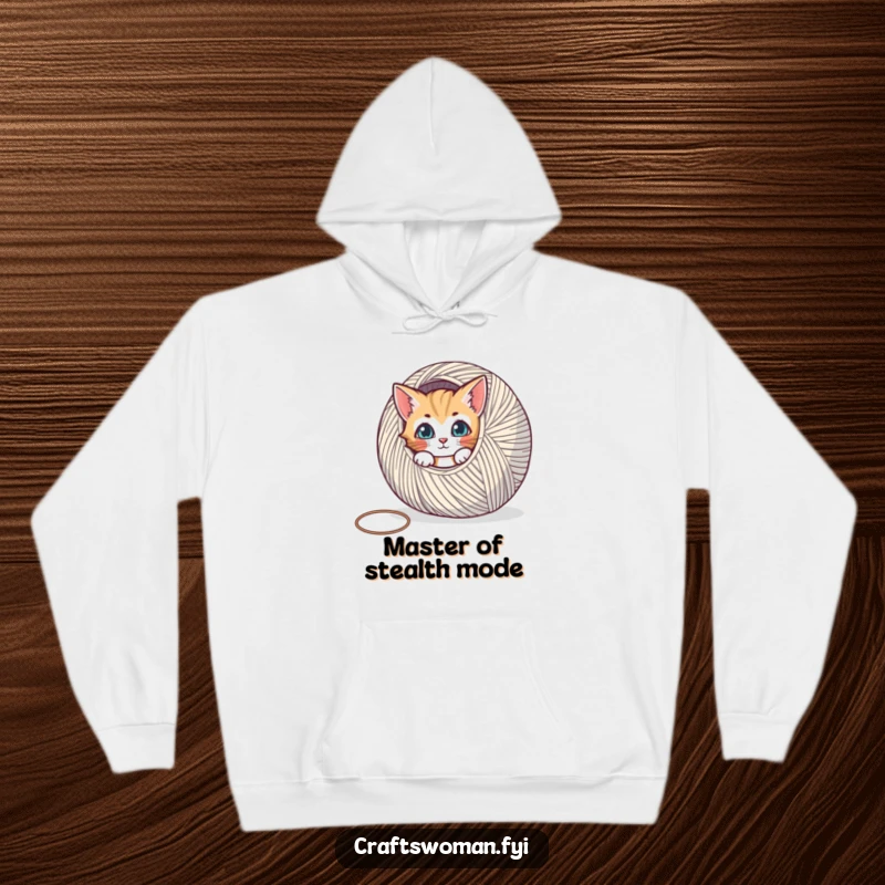 Funny hoodie depicting a curious cat peeking from behind a massive ball of yarn, perfect for cozy crafting sessions.